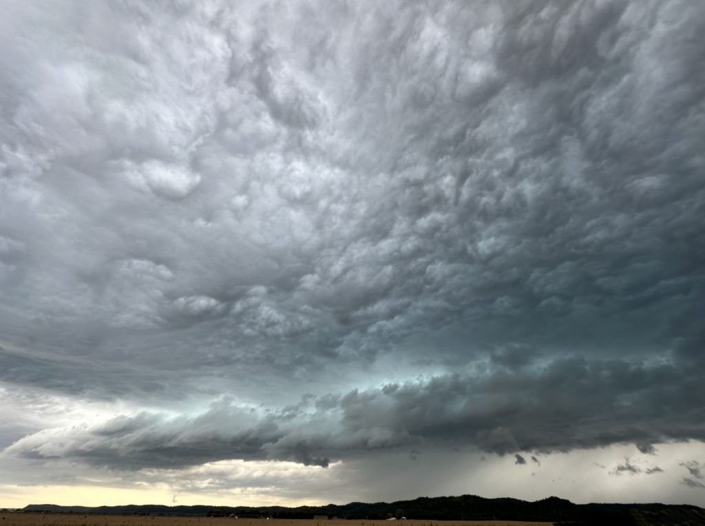 A photo of a thunderstorm complex above a farm field.