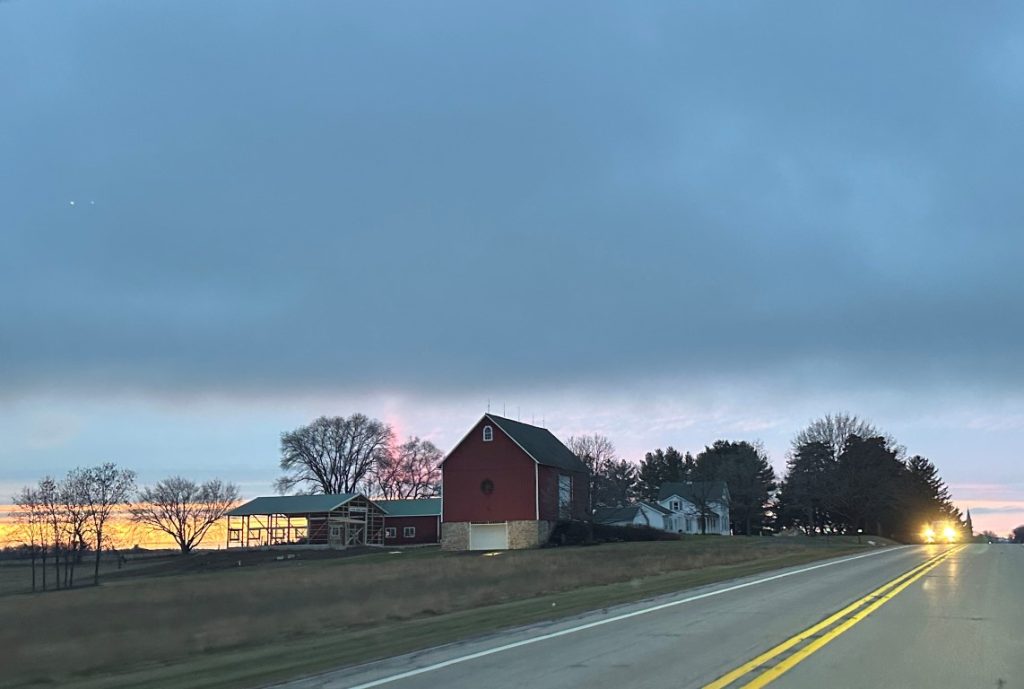 A photo of a barn along a rural road at sunset